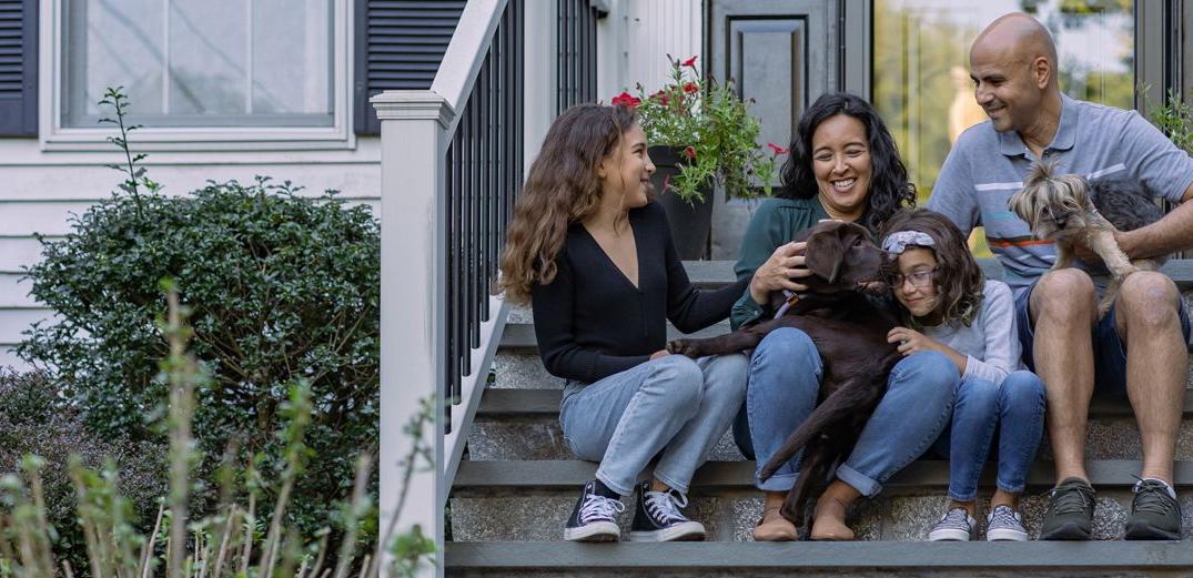 A family of four- plus their two dogs - sit on their front stoop.